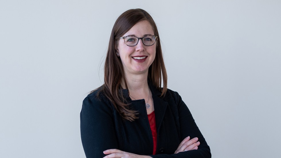 Cassandra Glynn is wearing glasses and a black jacket. She has long brown hair. 