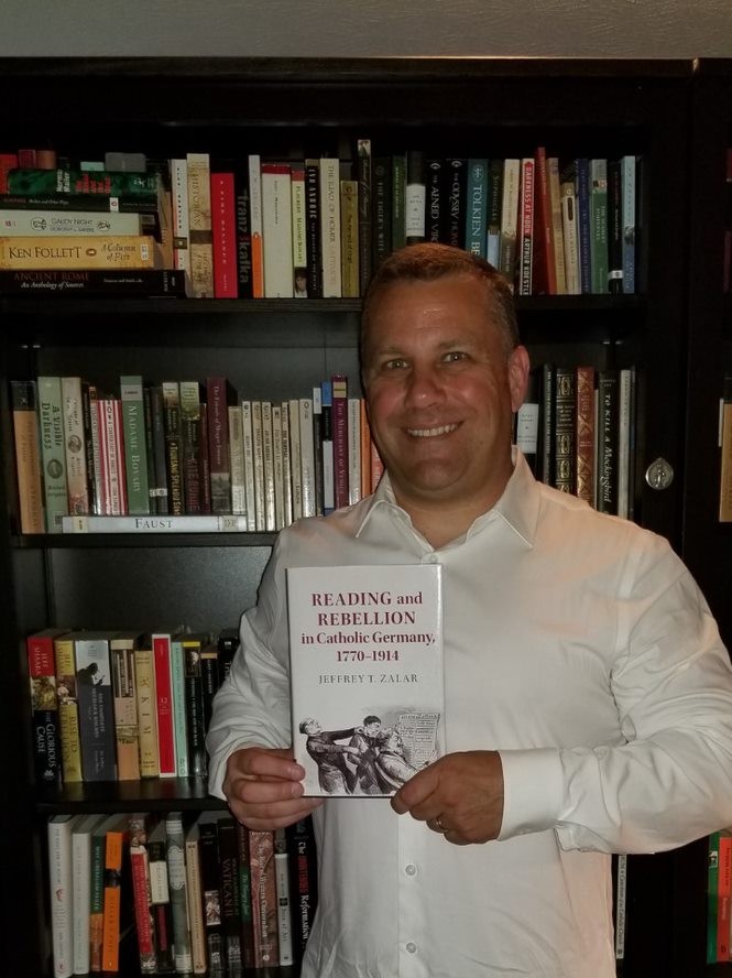 Man holding book smiling at camera 