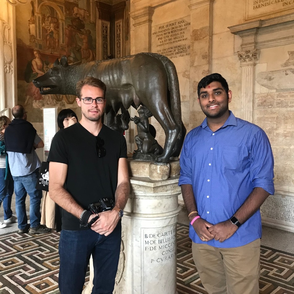 Two students pose in front of a statue of the Capitoline Wolf.