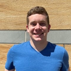 A smiling photo of Steven Quarin wearing a blue shirt outside in front of a stone background.