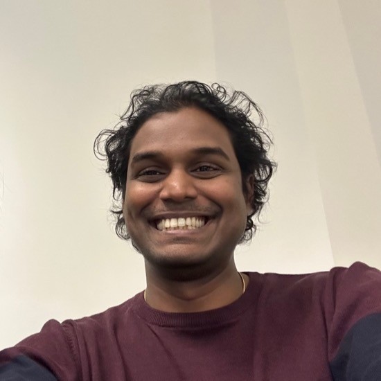 A smiling photo of Gayashan Rasanjana Jayavilal with black hair, with a dark red shirt in front of a light beige background.