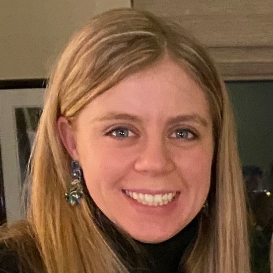 A smiling close up color photo of Jordan Siebold wearing a black shirt and dangling earrings.