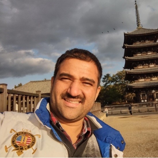 A smiling photo of Rohit Pal Singh with dark hair wearing an embroidered jacket with decorative architecture and clouds in the background.