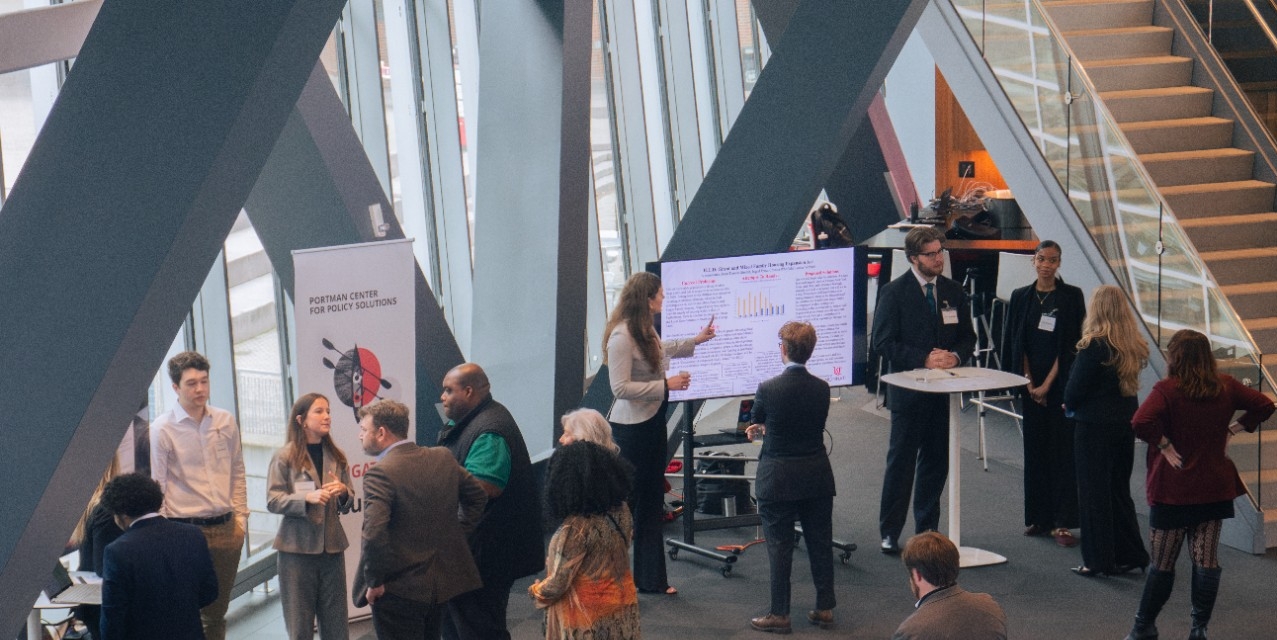 A modern conference room with people networking around presentation boards. Attendees are engaged in discussions, creating a professional and dynamic atmosphere.
